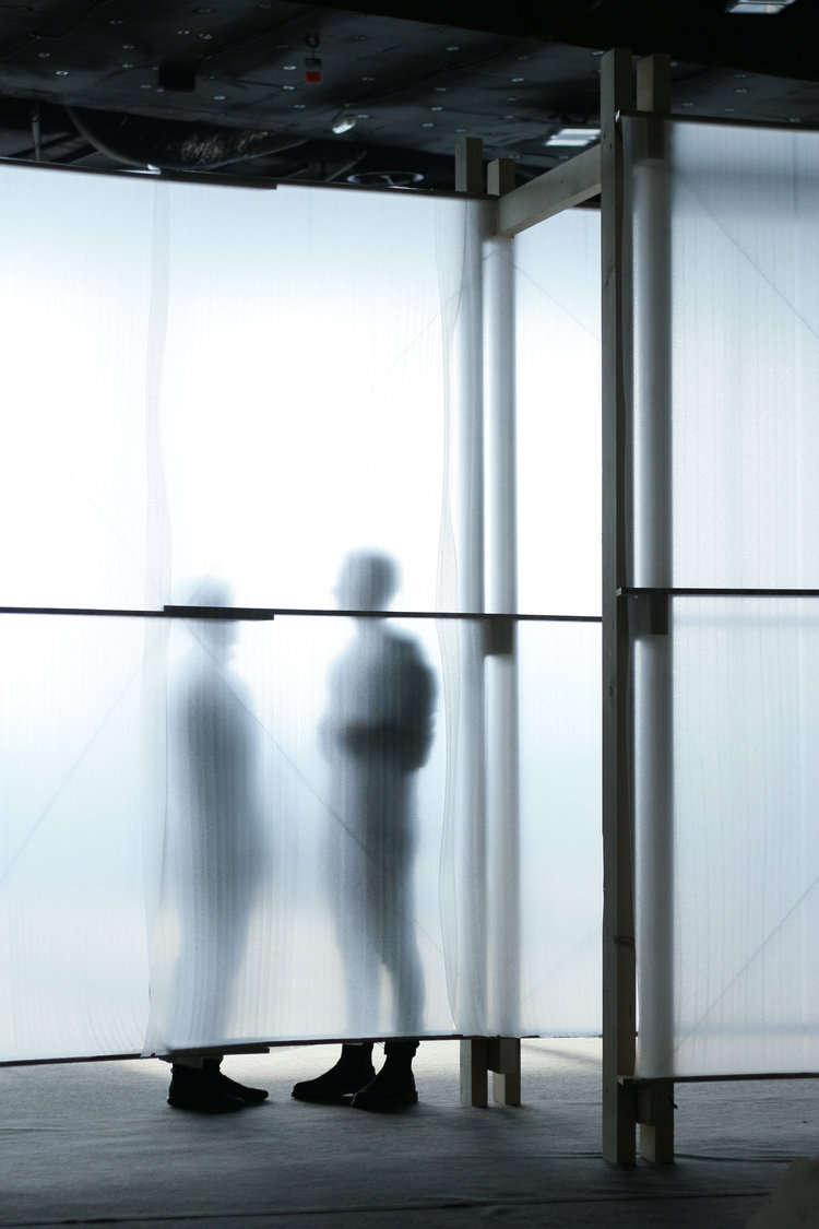 Two people talking seen through the semi-translucent walls of the pavilion.
